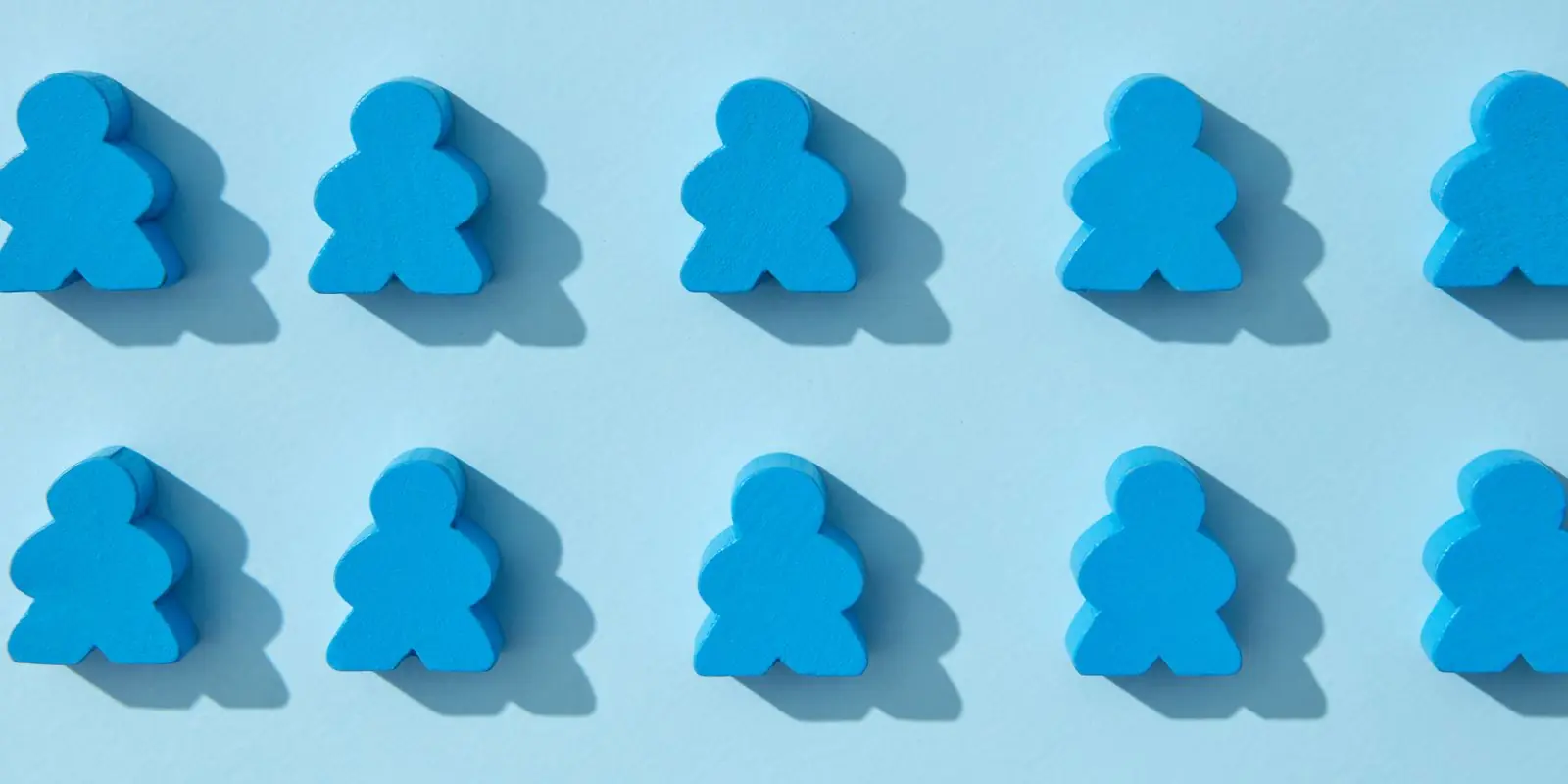 Two neat rows of identical blue wooden meeples casting shadows on a pale blue background