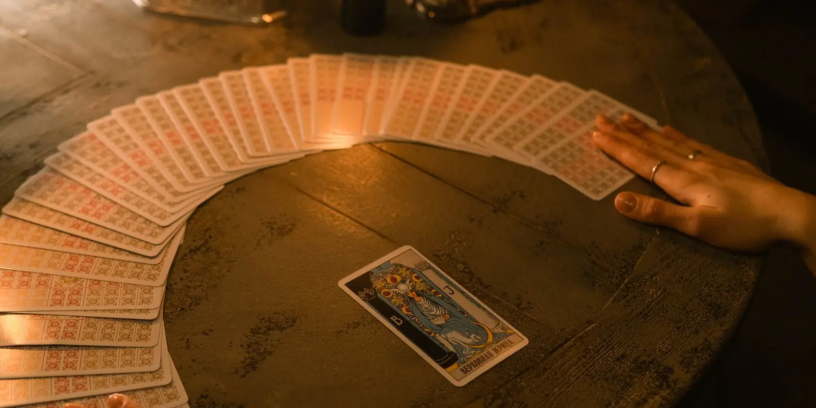 A deck fanned in a wide arc by candlelight with one illustrated card turned face up