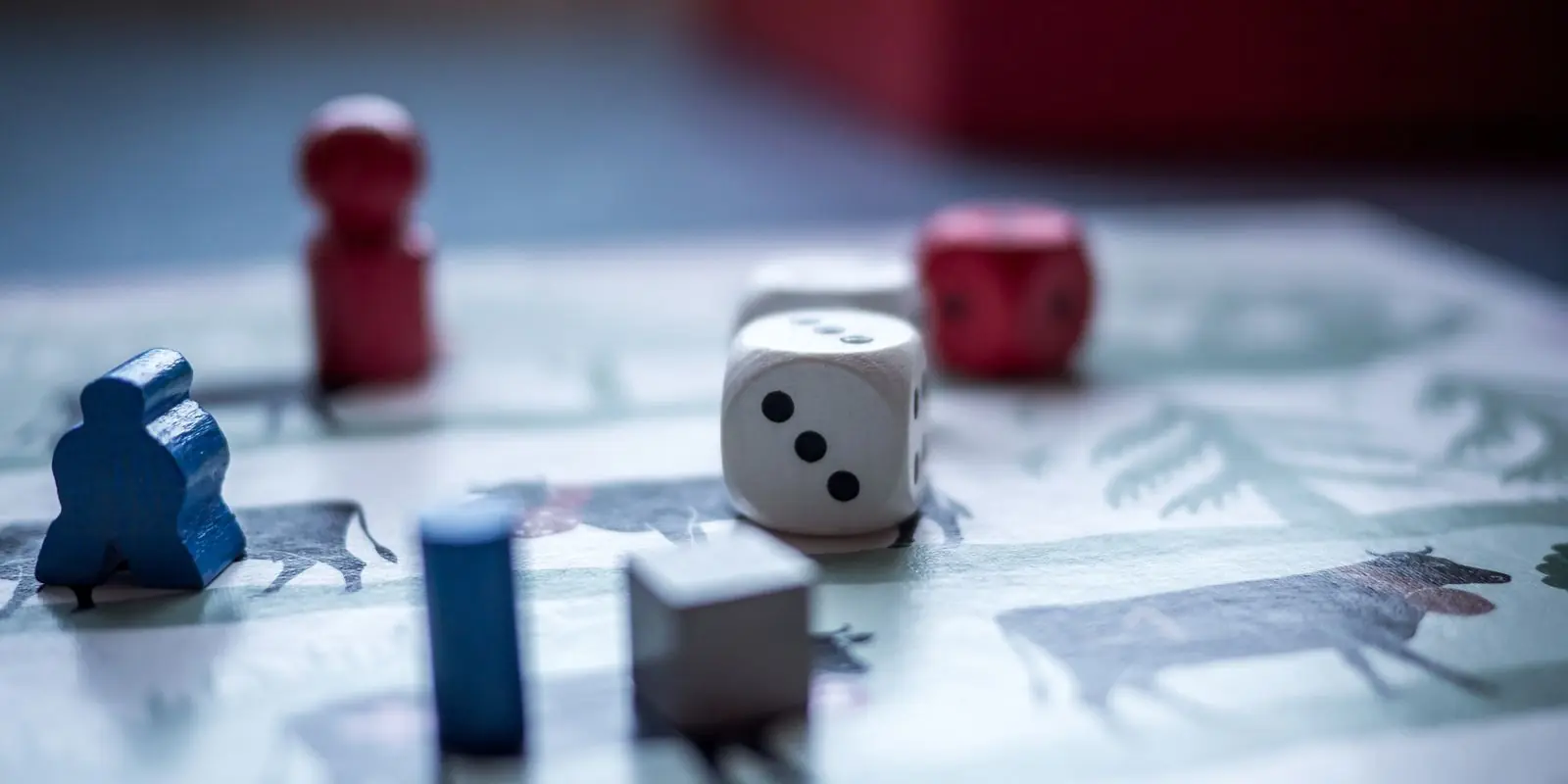 A blue wooden meeple, pawns, cubes and dice standing on an illustrated game board in close-up