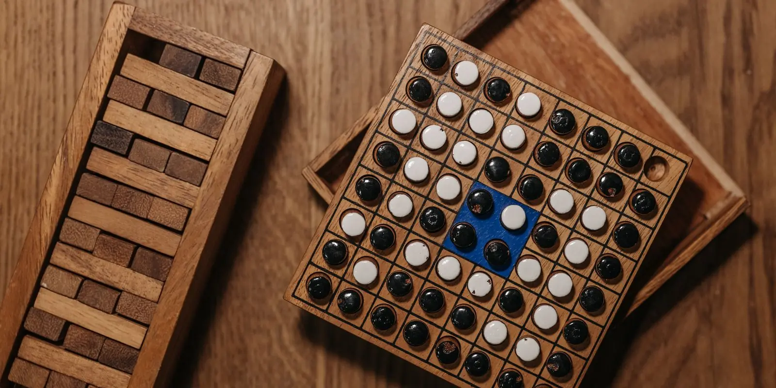 A wooden strategy board covered in black and white counters beside a stacked wooden block tower