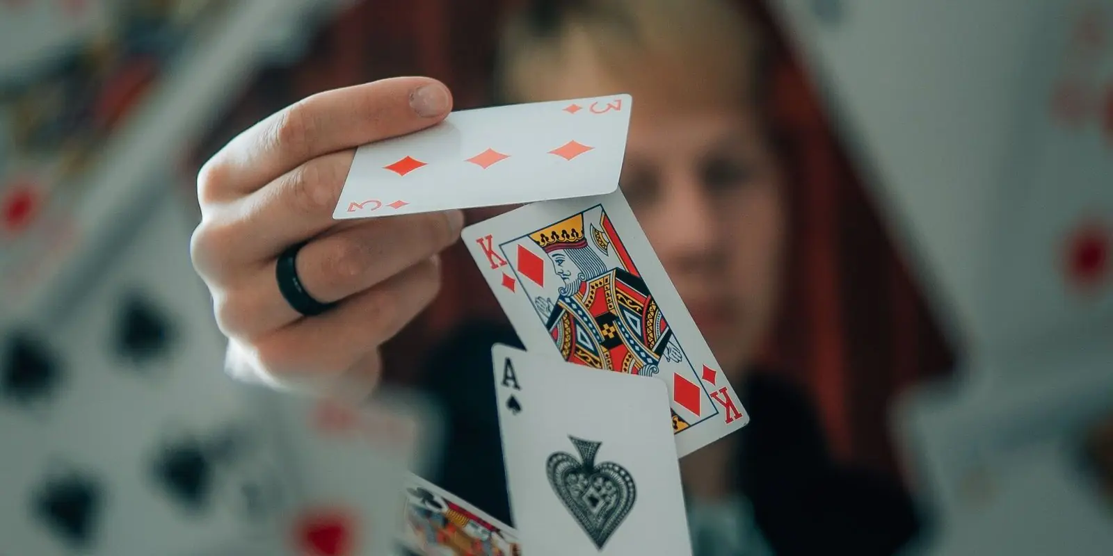A hand tossing playing cards towards the camera, with a three of diamonds, a king and an ace mid-air